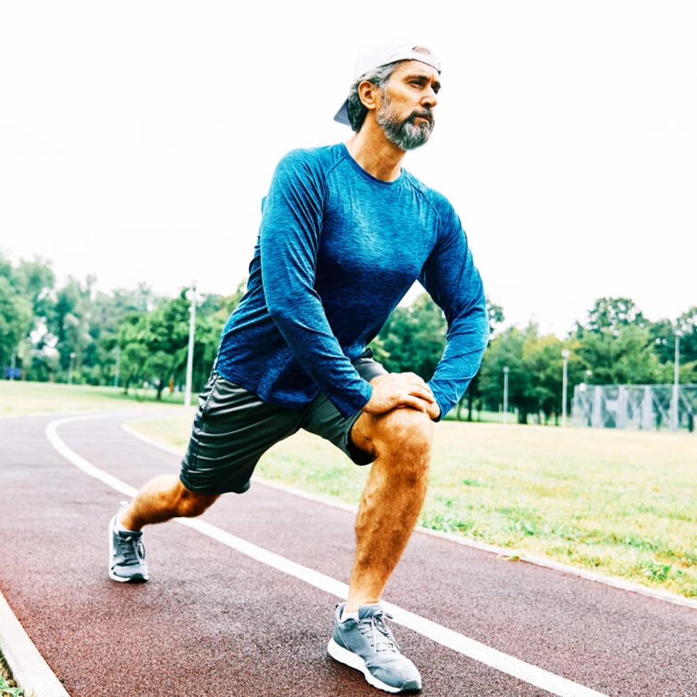 NAD Therapy Muscle Recovery Man stretching track Bionworx Carmel Man stretching on a running track before a workout, representing enhanced muscle recovery, energy, and cellular health from NAD+ Therapy at BionwoRx in Carmel, Indiana.
