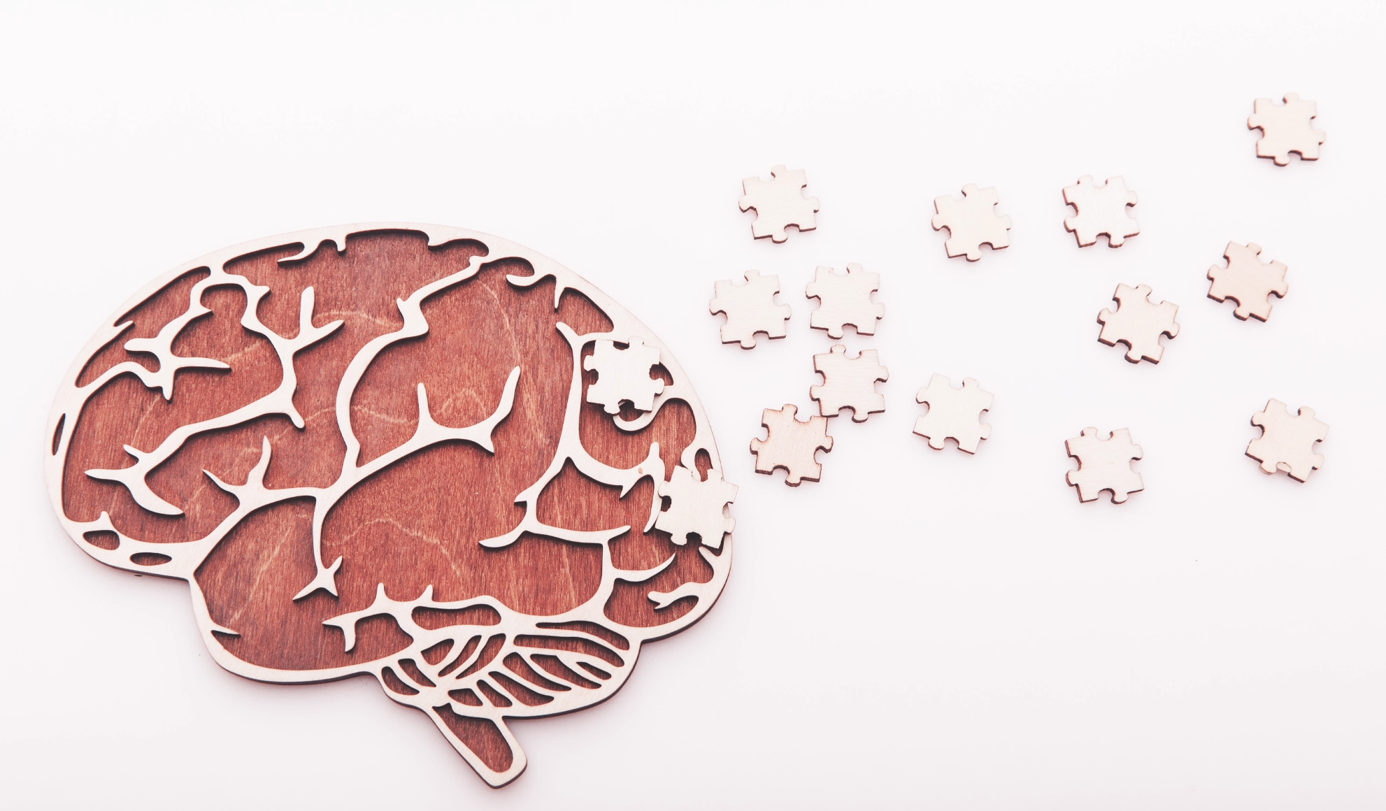 Wooden brain cutout with missing jigsaw puzzle pieces symbolizing memory loss and cognitive decline associated with Alzheimer’s disease and dementia